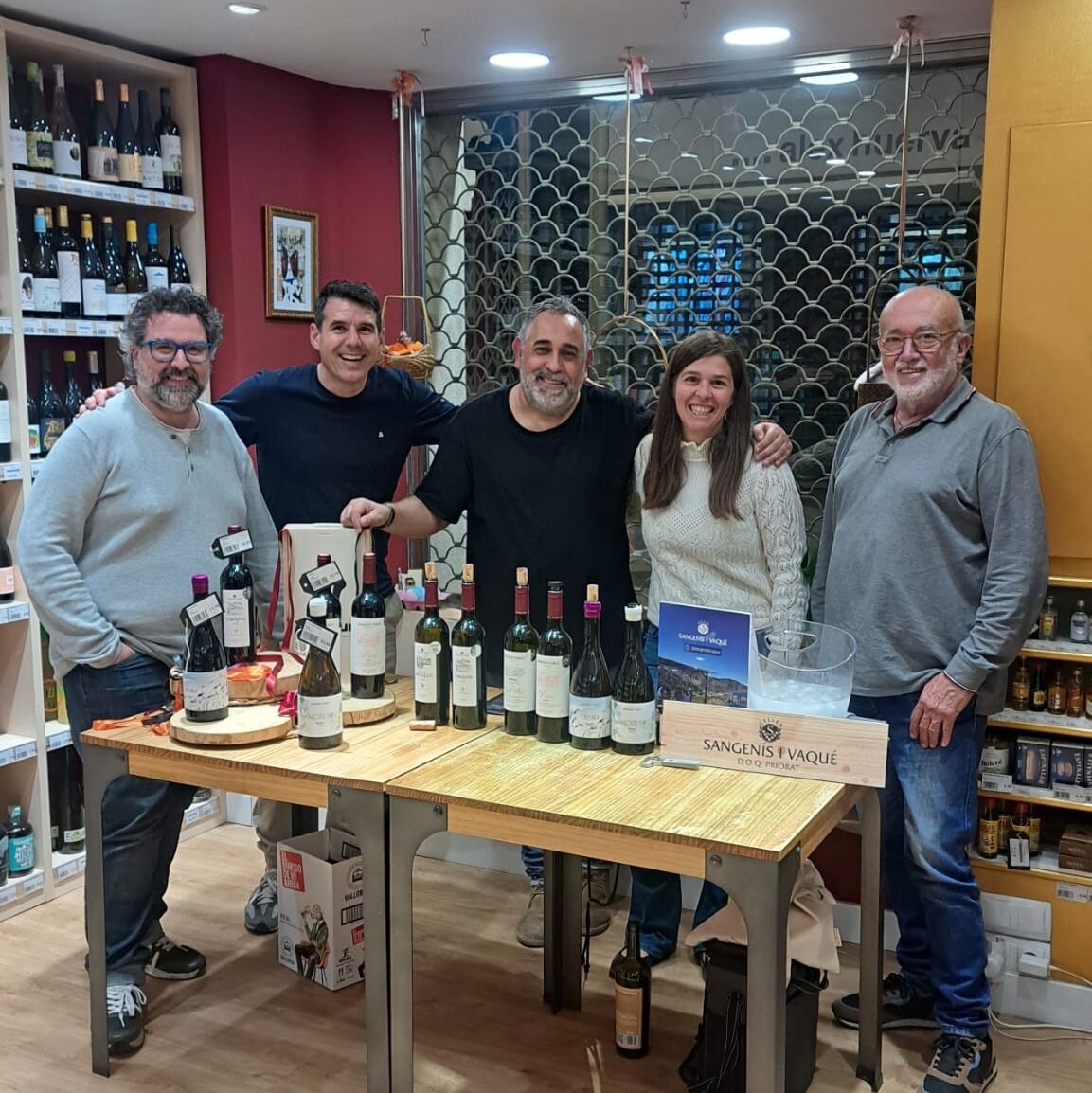 Retrat de grup somrient de l'equip de Vinalium Manresa i els elaboradors del celler Sangenís i Vaqué al voltant d'una taula de tast. La taula està plena d'ampolles de vi negre i blanc, algunes a sobre de rodanxes de fusta, a punt per ser tastades.