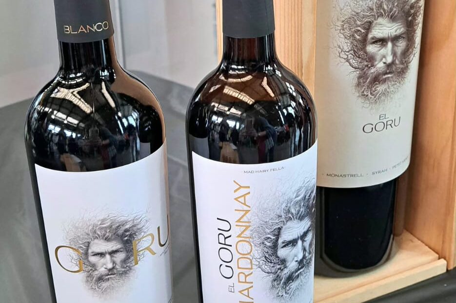 Dues ampolles de vi negre Goru de Ego Bodegas (DO Jumilla) presentades juntes. Destaquen per les seves etiquetes modernes i artístiques amb el rostre d'un home amb barba de traç ràpid i estil grafit sobre fons blanc. Una de les etiquetes té detalls en tons blaus i l'altra en tons vermells o granats