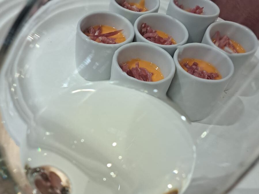 Copa de vi blanc Nonell Blanc de Noirs en primer pla, mostrant al fons uns gots de salmorejo per a un maridatge gastronòmic.